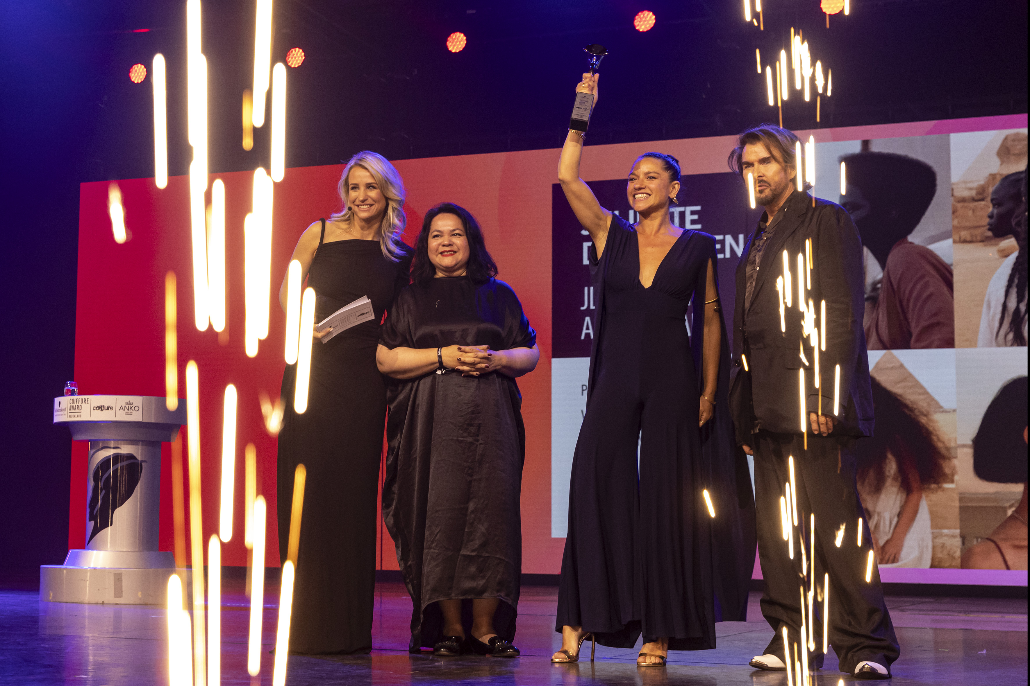 Juliette den Ouden wint een Coiffure Award, trofee omhoog houdend op het podium