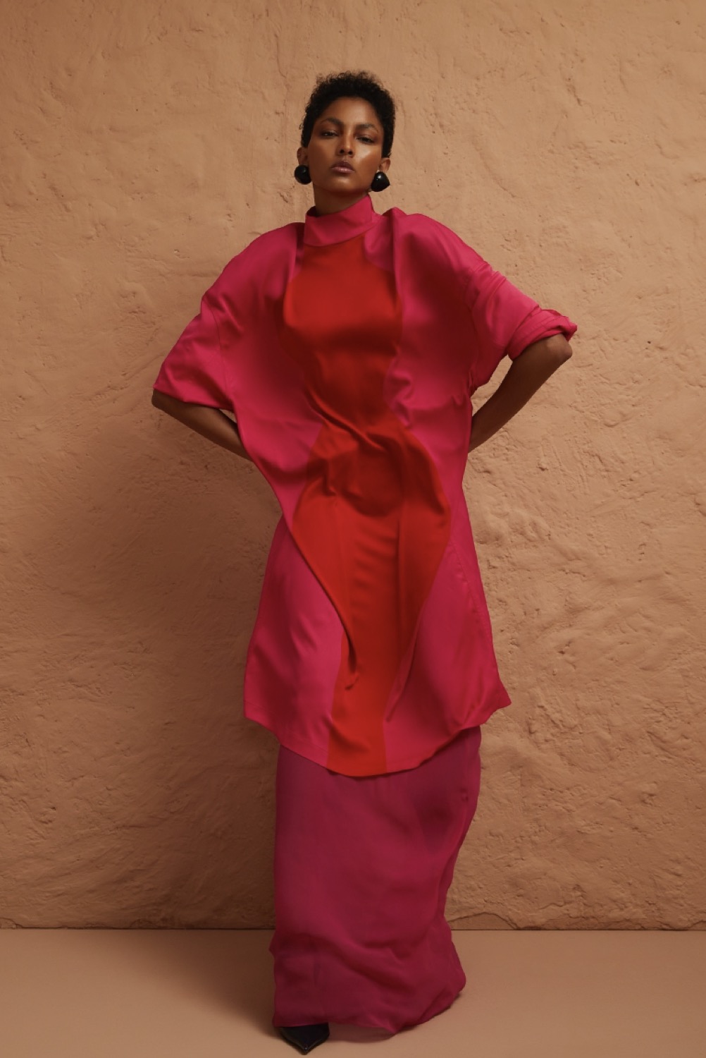 Hair & make-up voor Glamour editorial, model in rood-roze jurk tegen terracotta muur