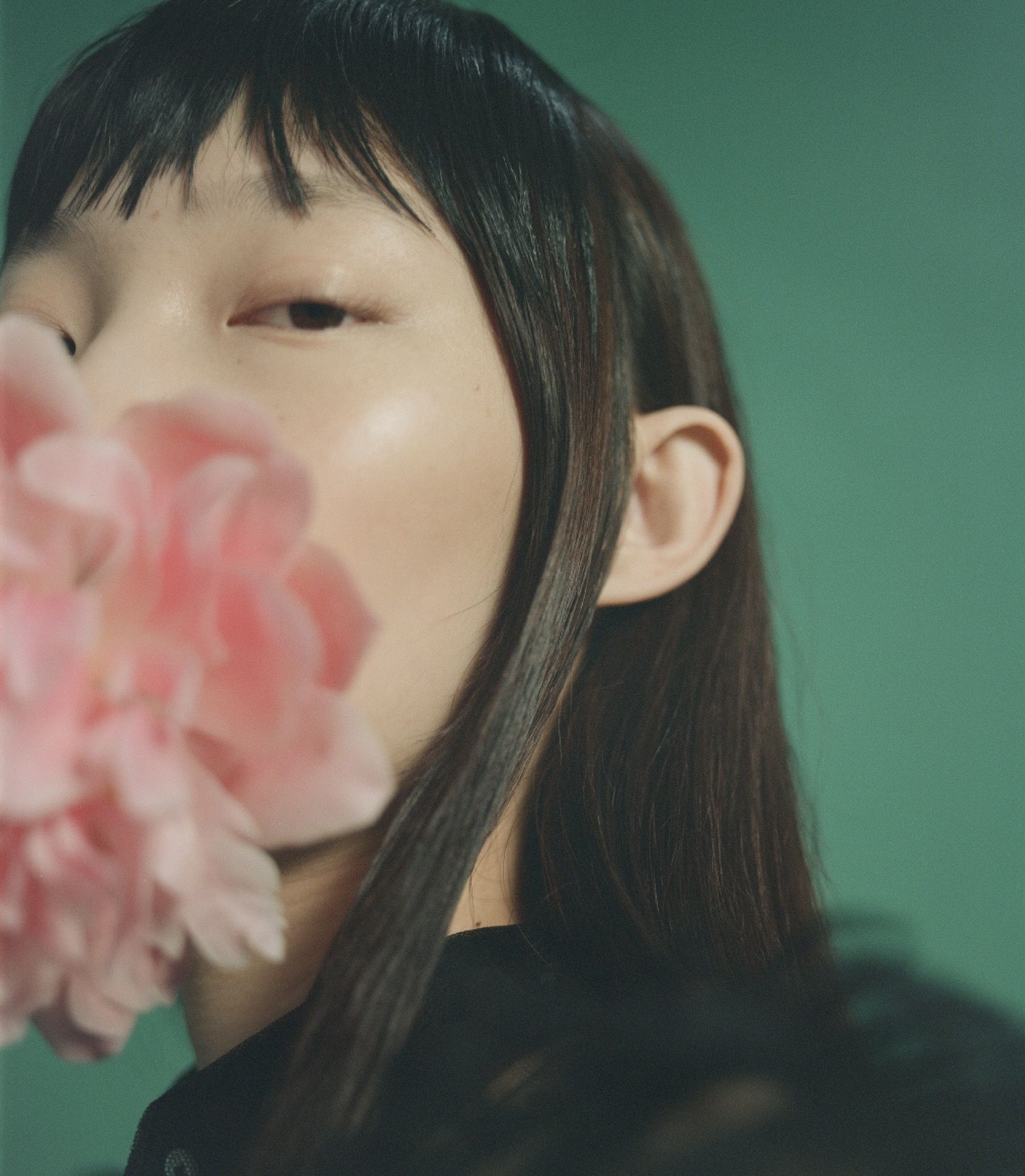Beauty editorial, half gezicht tegen teal met roze pioenroos